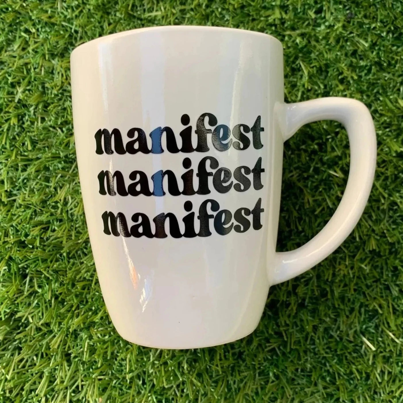 White mug with manifest manifest manifest on a green grass background